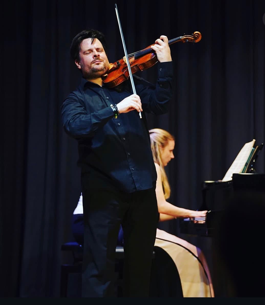 Violinist performing on stage with piano accompaniment